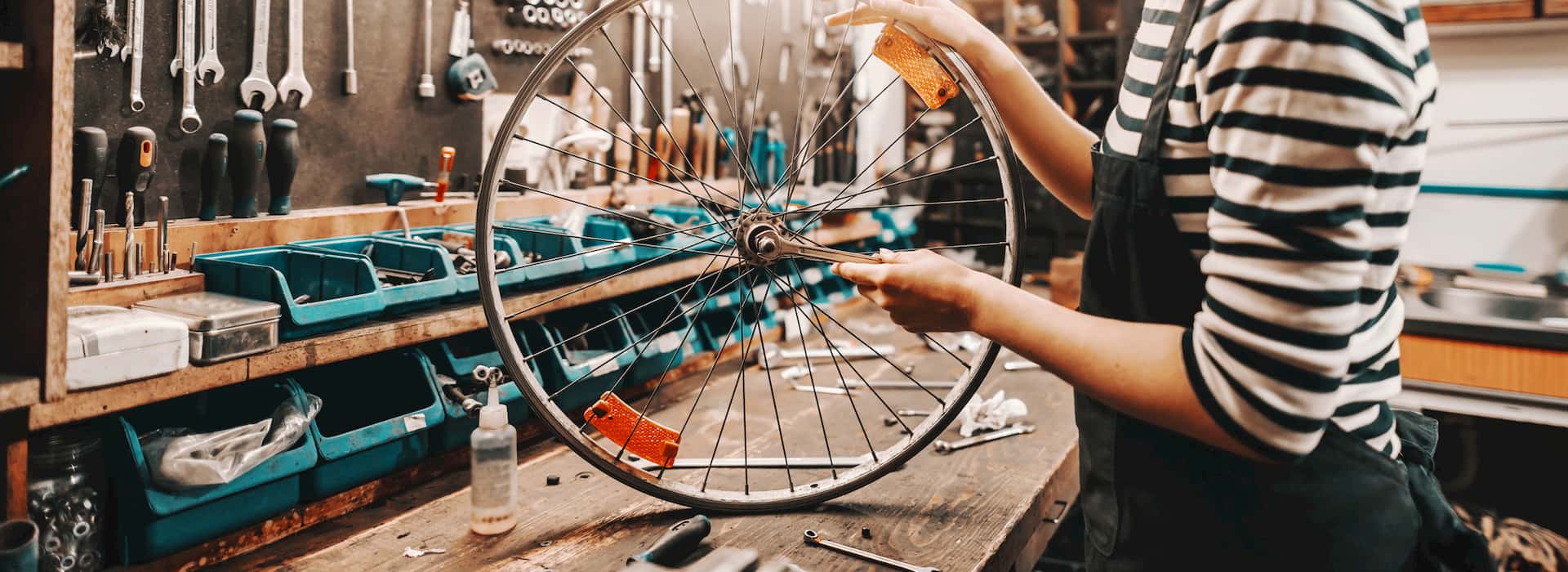 Cute Caucasian female worker holding and repairing bicycle wheel while standing in bicycle workshop. © Adobe Stock